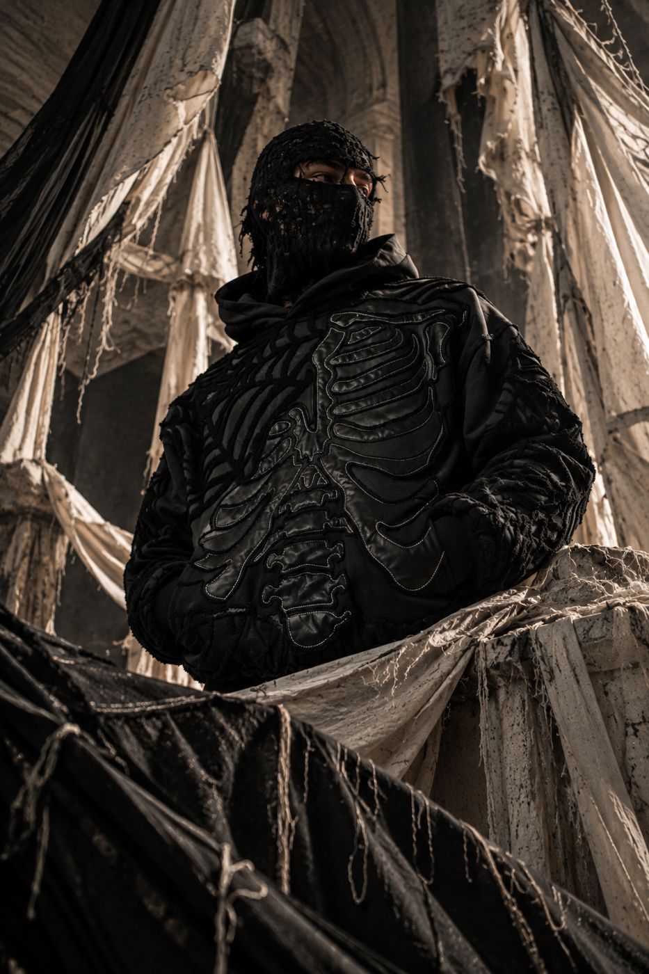 Figure in all black and a black mask among torn drapes